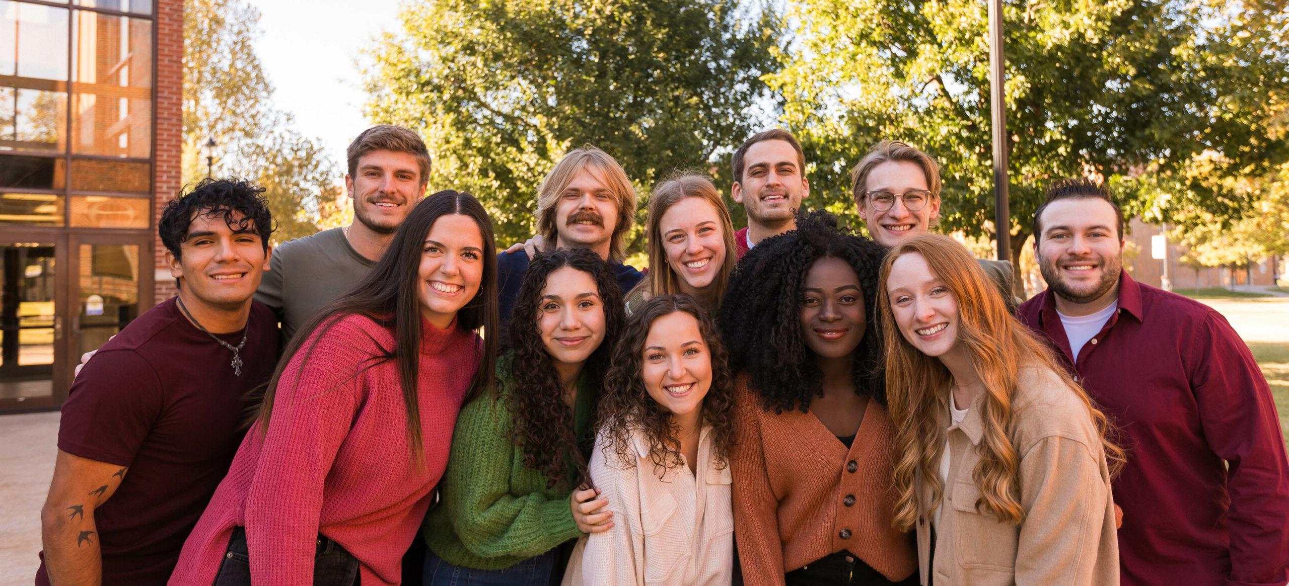 A diverse group of SNU students standing on the campus of SNU smiling, dressed in fall colors